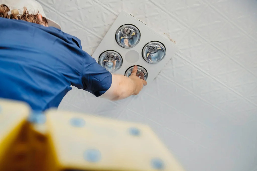 Technician replacing halogen downlight globes with LED globes in Perth home.