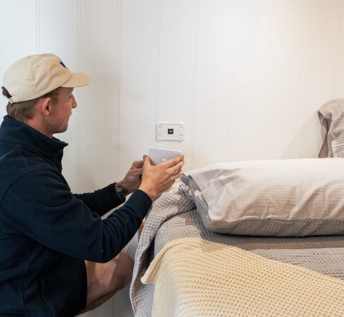 Electrician installing air conditioning system near bed in Perth home setting.